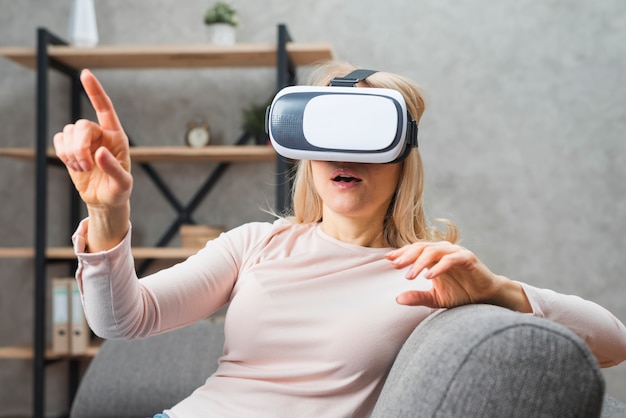 Foto grátis jovem, mulher, usando um fone de ouvido de realidade virtual, apontando o dedo para algo