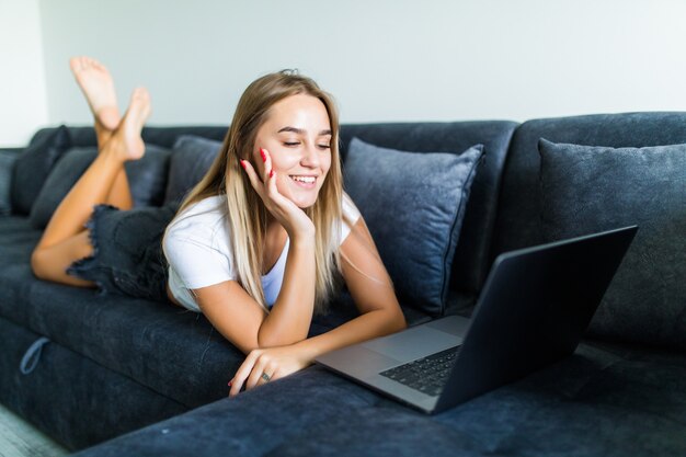 Jovem mulher usando um laptop enquanto relaxa no sofá