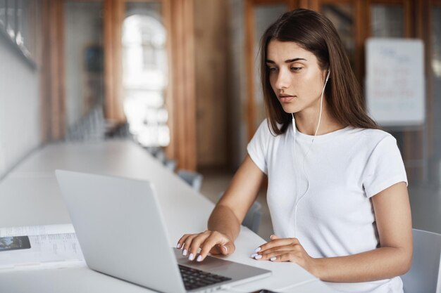 Jovem mulher usando um notebook assistindo filmes ou ouvindo música online no campus universitário