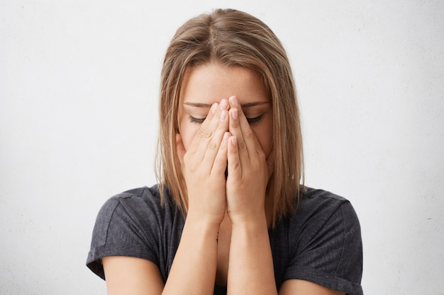 Foto grátis jovem mulher vestida casualmente cobrindo o rosto com as duas mãos, sentindo-se nervosa ou envergonhada, sem olhar, escondendo-se. expressões faciais humanas, emoções, sentimentos, reações e atitudes