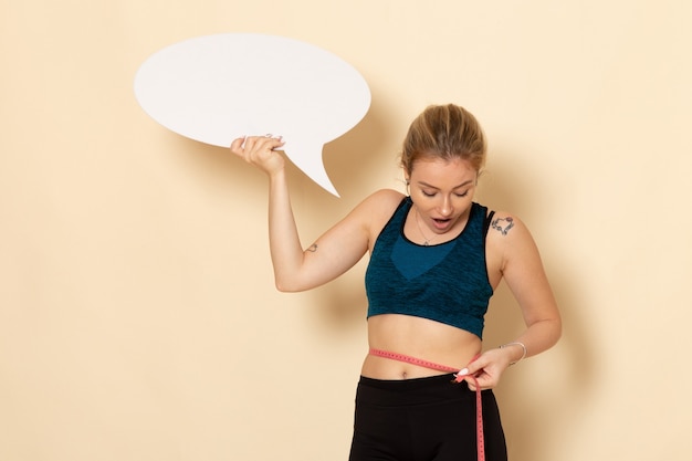 Jovem mulher vestida de frente com roupa esporte, segurando uma placa branca e medindo o corpo