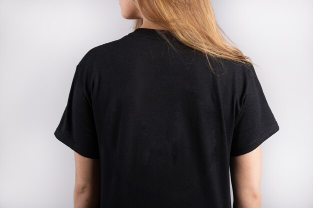 Jovem mulher vestindo uma camiseta preta de manga curta com uma parede branca ao fundo