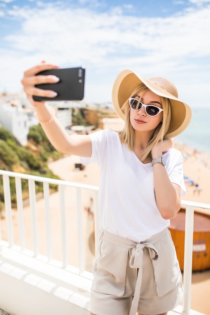 Jovem mulher viajando segurando um telefone fazendo selfie contra o mar