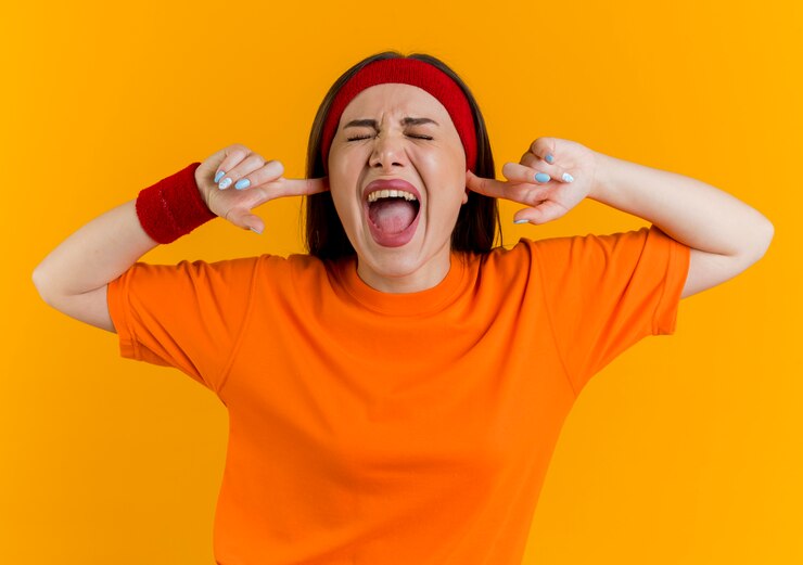 Foto grátis jovem mulher zangada e esportiva usando bandana e pulseiras, mantendo as mãos nos ouvidos, gritando com os olhos fechados