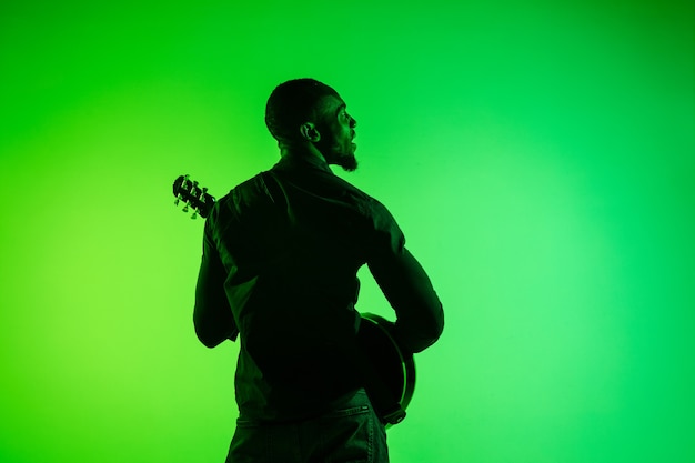 Jovem músico afro-americano tocando guitarra como uma estrela do rock em fundo gradiente verde-amarelo.