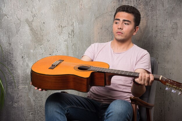 Jovem músico olhando guitarra em fundo de mármore