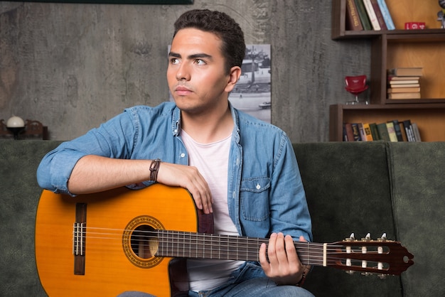 Jovem músico segurando a guitarra e sentado no sofá. foto de alta qualidade