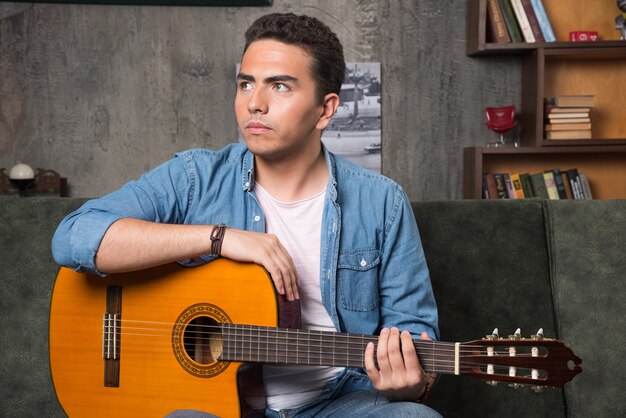 Jovem músico segurando a guitarra e sentado no sofá. Foto de alta qualidade