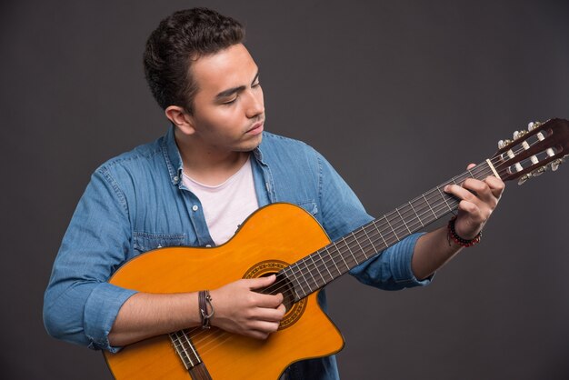 Jovem músico tocando guitarra em fundo preto. Foto de alta qualidade