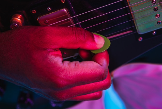 Jovem músico tocando violão como uma estrela do rock sobre fundo azul em luz de néon.