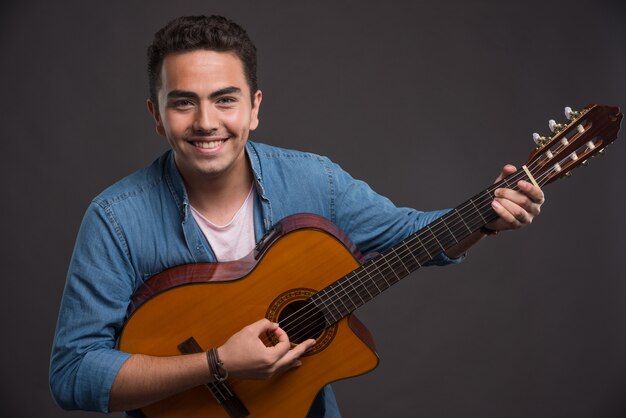 Jovem músico tocando violão em fundo preto