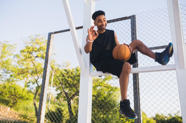 Jovem negro praticando esportes, jogando basquete, estilo de vida ativo, manhã de verão, sorrindo feliz se divertindo