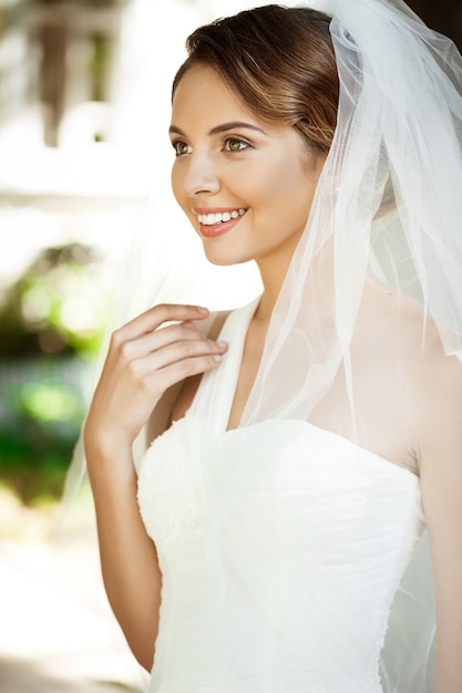 Jovem noiva loira linda no vestido de casamento e véu sorrindo.