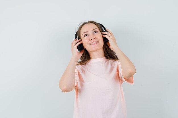 Jovem numa t-shirt rosa curtindo música com fones de ouvido e olhando alegre, vista frontal.