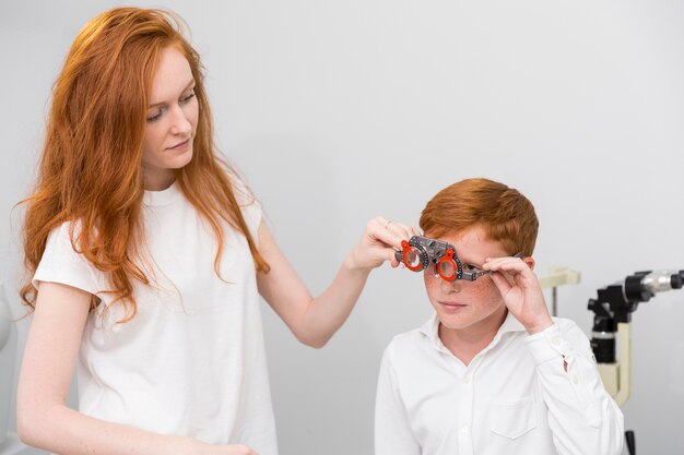 Jovem oculista feminina usando quadro experimental de optometrista para menino bonito para verificar seus olhos