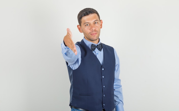 Jovem, oferecendo a mão para apertar um terno, jeans e parece amigável.