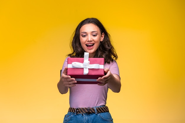 Jovem, oferecendo uma caixa de presente vermelha e sorrindo.