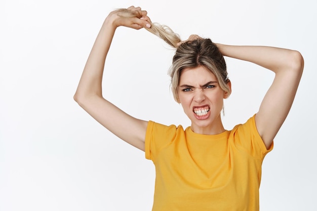 Jovem olhando com raiva puxando o cabelo e apertando os dentes conceito de cuidados capilares e produtos cosméticos em camiseta amarela contra fundo branco