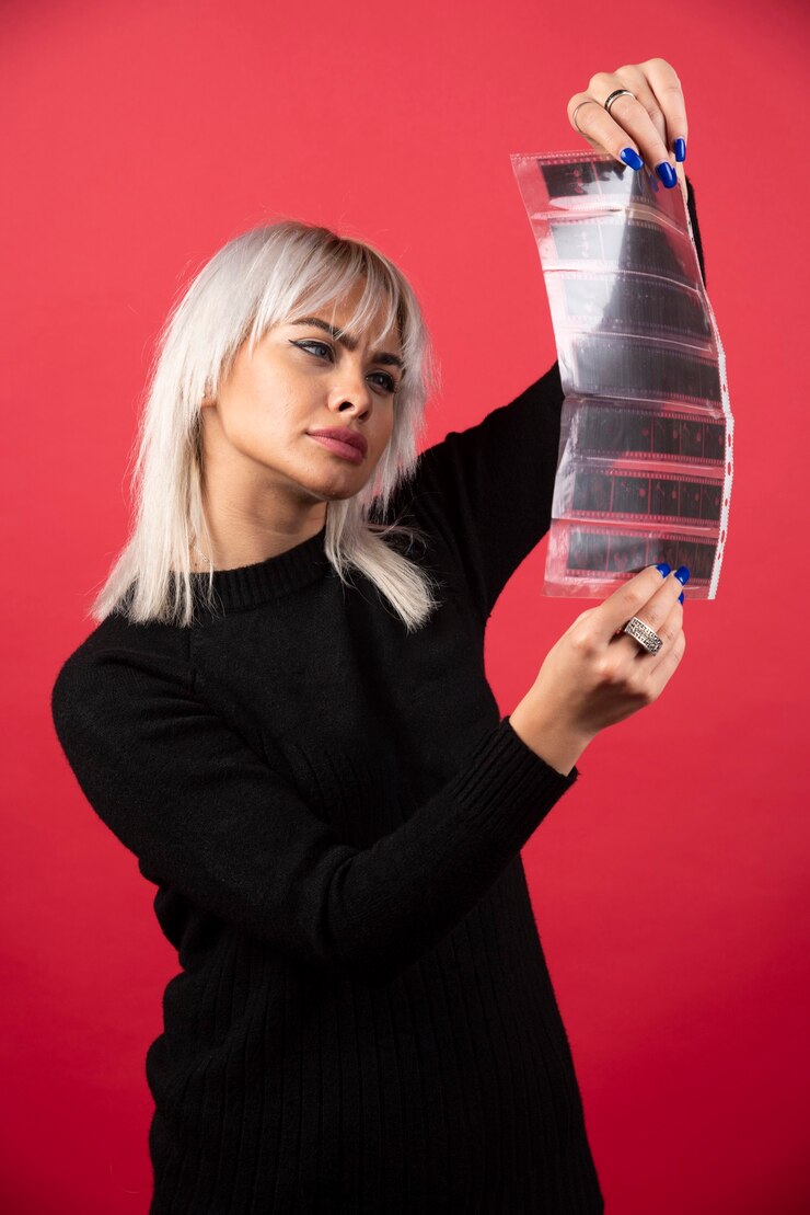 Foto grátis jovem olhando em uma fita fotográfica em um fundo vermelho. foto de alta qualidade