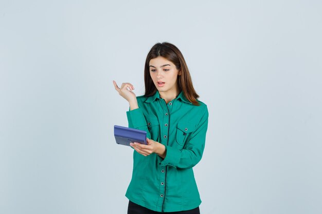 Jovem olhando para a calculadora enquanto mostra o gesto eureka na camisa verde e parecendo surpresa. vista frontal.