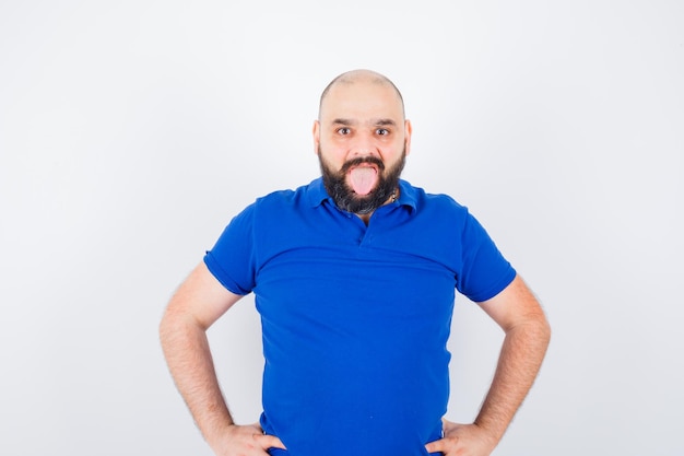 Jovem olhando para a câmera com a mão na cintura, mostrando a língua na vista frontal da camisa azul.