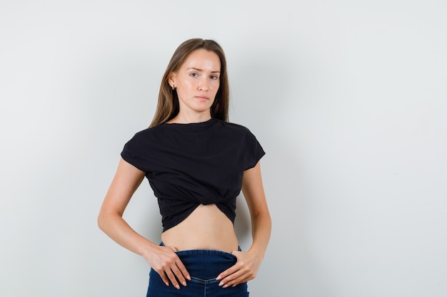 Jovem olhando para a câmera de blusa preta, calça e olhando sério.