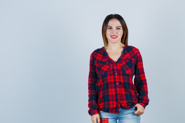 Jovem olhando para a frente em uma camisa xadrez e parecendo alegre. vista frontal.