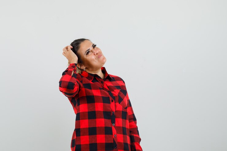 Foto grátis jovem olhando para cima enquanto coça a cabeça com uma camisa quadriculada e parecendo sonhadora