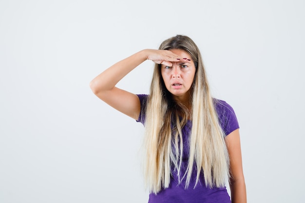 Jovem, olhando para longe com a mão na cabeça em t-shirt violeta e parecendo cansada, vista frontal.