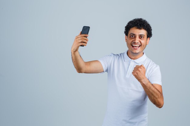 Jovem olhando para o celular em uma camiseta branca e parecendo feliz. vista frontal.