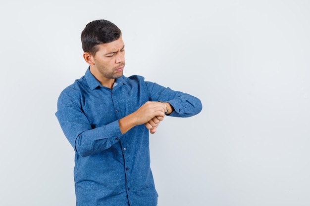 Foto grátis jovem olhando para o relógio de camisa azul e olhando preocupado, vista frontal.