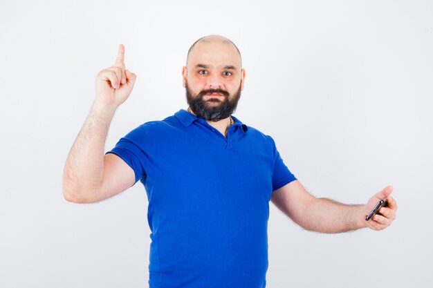 Jovem olhando para o telefone enquanto aponta para cima na vista frontal de camisa azul.