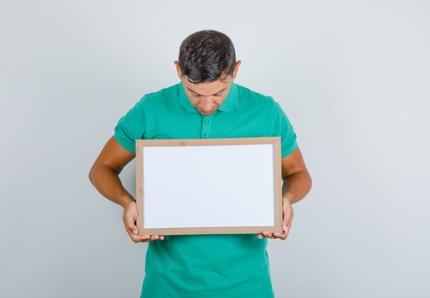 Foto grátis jovem olhando para quadro branco em t-shirt verde, vista frontal.