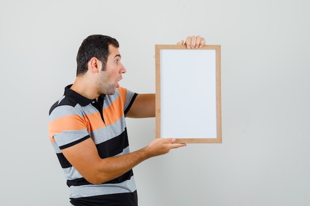 Foto grátis jovem olhando para um quadro em branco em uma camiseta e parecendo pasmo