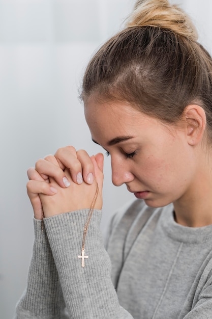 Jovem orando em casa com colar de cruz