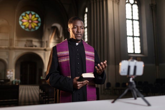 Foto grátis jovem padre masculino transmitindo o sermão da igreja com smartphone