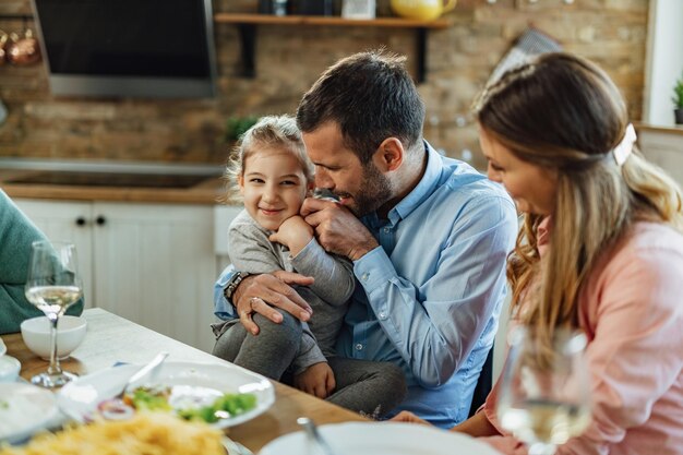 Jovem pai se divertindo com sua filha e fazendo cócegas durante o almoço na mesa de jantar