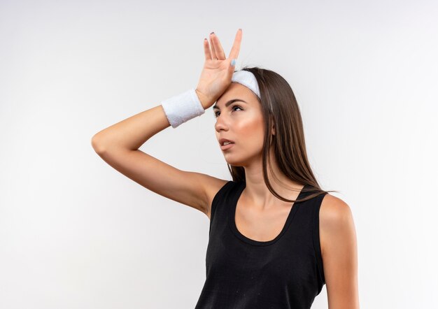 Foto grátis jovem pensativa e muito esportiva usando bandana e pulseira, colocando a mão na cabeça e olhando para cima no espaço em branco