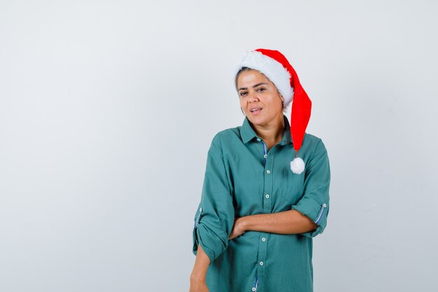 Jovem, posando com chapéu de natal, camiseta e olhando cuidadosa, vista frontal.