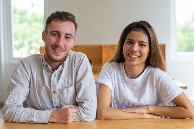 Jovem positivo e mulher sentada à mesa e posando