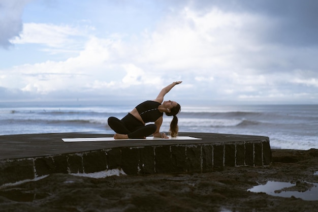 Jovem pratica ioga em uma bela praia ao nascer do sol. Céu azul, mar, ondas, proximidade com a natureza, união com a natureza.