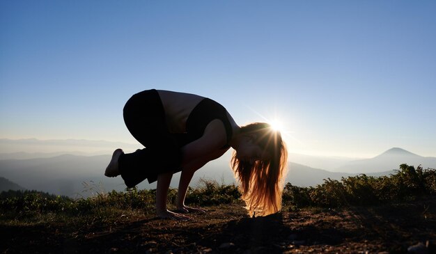 Jovem praticando ioga durante o pôr do sol nas montanhas