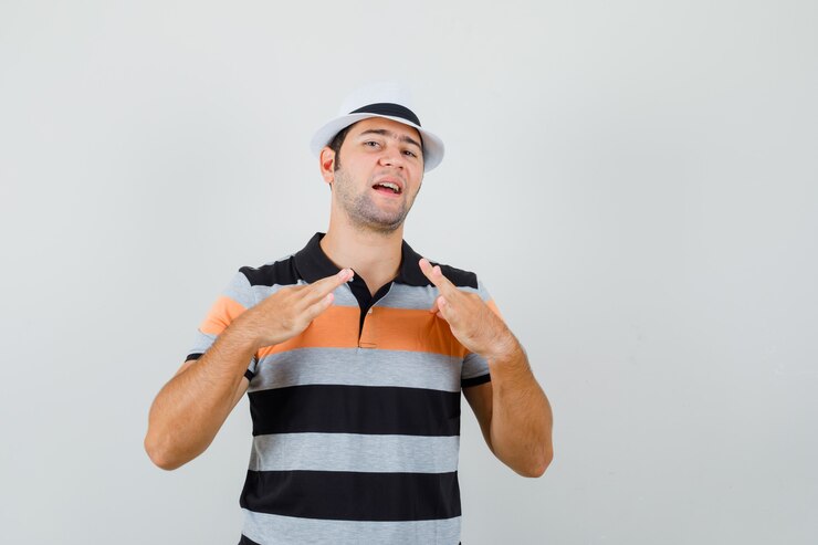 Foto grátis jovem puxando sua t-shirt ligeiramente na t-shirt, chapéu e parecendo entediado, vista frontal.