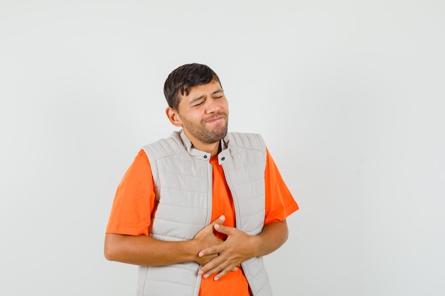 Foto grátis jovem que sofre de dor de estômago em uma camiseta, jaqueta e parece desconfortável.