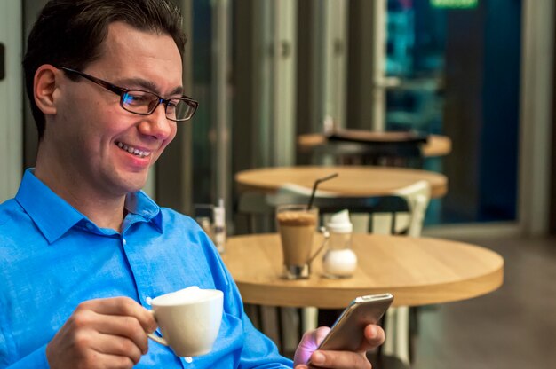 Jovem que texting no café. Feliz empresário sorrindo e texting no smartphone na mesa