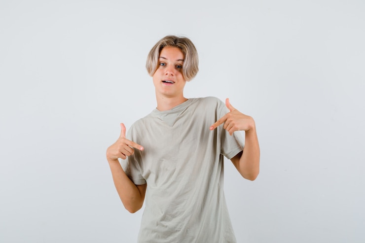 Foto grátis jovem rapaz adolescente em t-shirt, apontando para si mesmo e olhando alegre, vista frontal.
