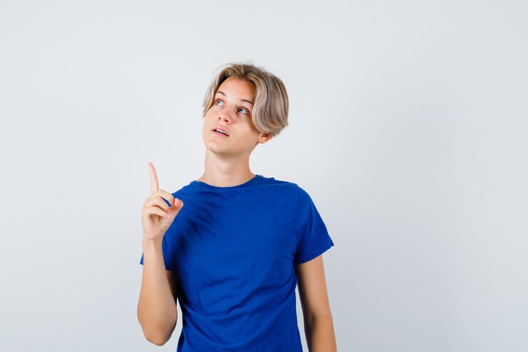 Foto grátis jovem rapaz adolescente em t-shirt azul apontando para cima, olhando para cima e parecendo esperançoso, vista frontal.