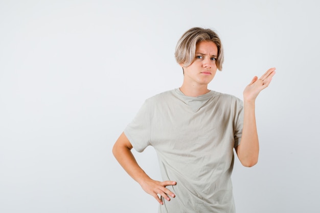 Jovem rapaz adolescente em t-shirt fingindo mostrar algo e olhando perplexo, vista frontal.