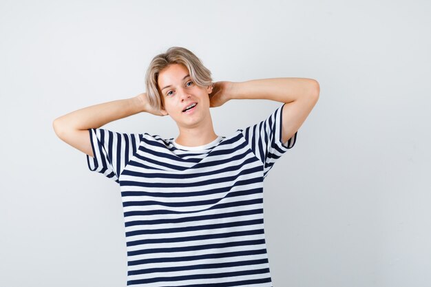 Jovem rapaz adolescente em t-shirt listrada com as mãos atrás da cabeça e olhando relaxado, vista frontal.