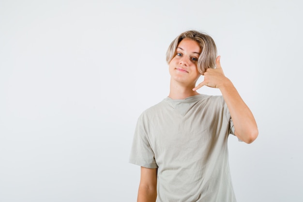 Jovem rapaz adolescente em t-shirt mostrando gesto de telefone e olhando alegre, vista frontal.